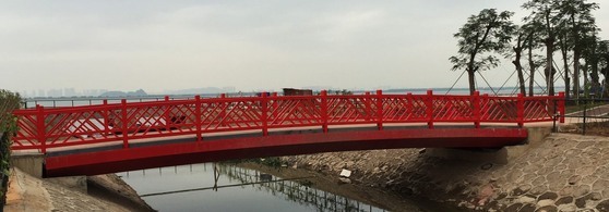 Red painted steel landscape pedestrian bridge over a waterway